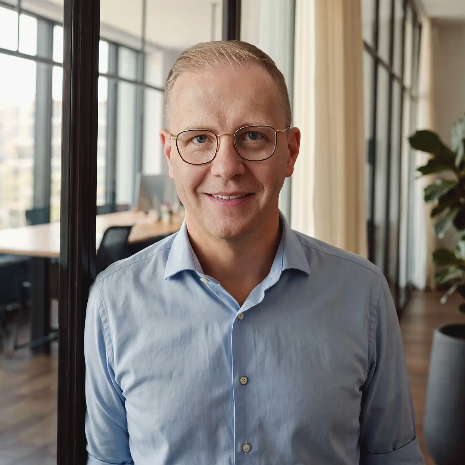 Porträt von Tim Hoferichter von Hoferichter Unternehmenssteuerrecht mit Brille und grauem Sakko in moderner Büroumgebung.