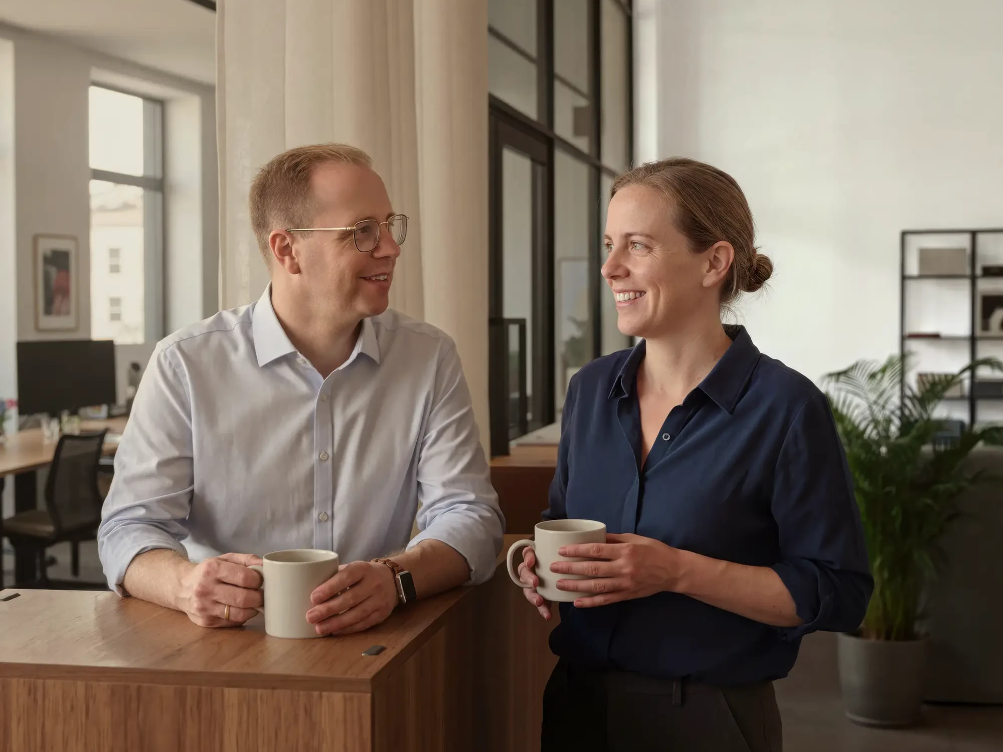 Tim Hoferichter im persönlichen Austausch mit einer Mitarbeiterin bei einer Kaffeepause in den modernen Büroräumen von Hoferichter Unternehmenssteuerrecht.
